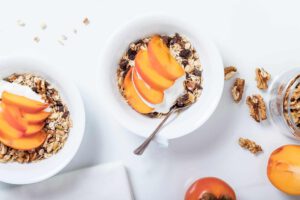 Two bowls of granola with yogurt and persimmon slices. Walnuts and a jar of granola are also visible.