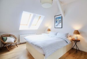 Cozy attic bedroom with white bed, skylights, and wood floors.