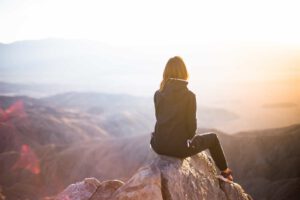 Woman sitting on a rock overlooking a vast mountain range at sunset.