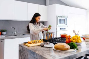 Woman cooking healthy meal in modern kitchen. She adds greens to a pot on the stove.