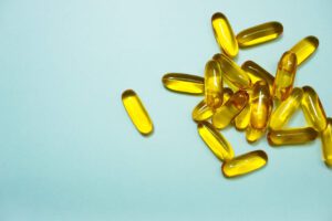 Pile of golden-yellow omega-3 fish oil capsules on a light-blue background.