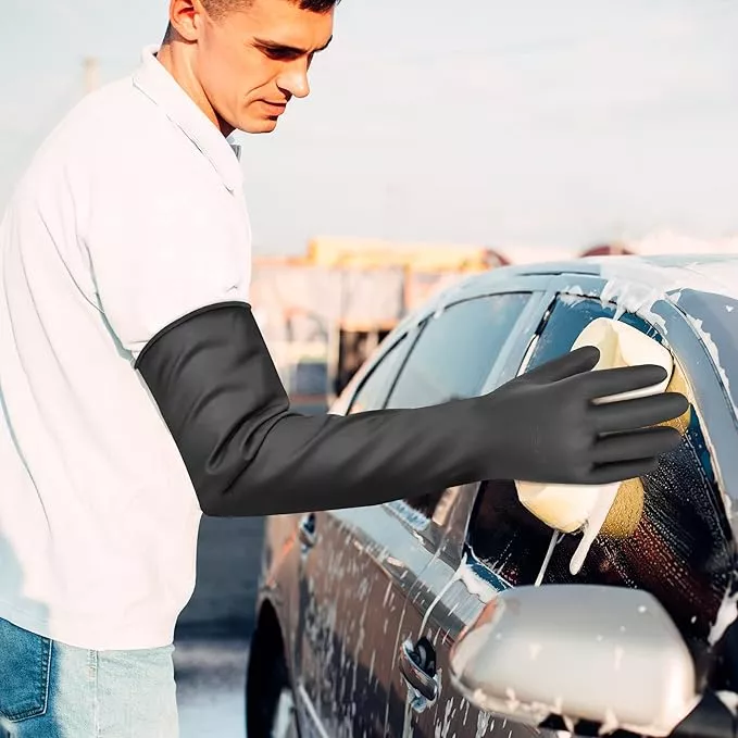 Man washing a car wearing long black protective gloves, preventing water from reaching his arms.