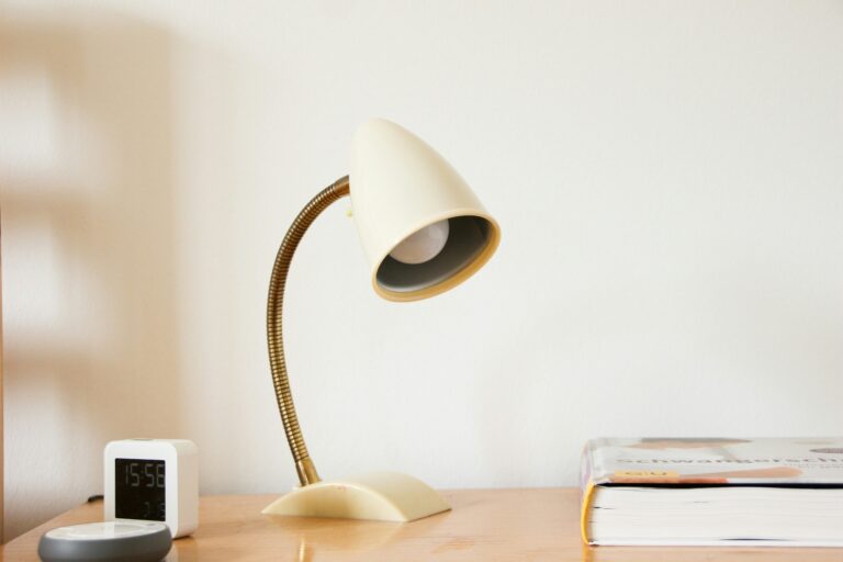 Vintage cream-colored desk lamp with a flexible neck on a wooden desk next to a digital clock and book.